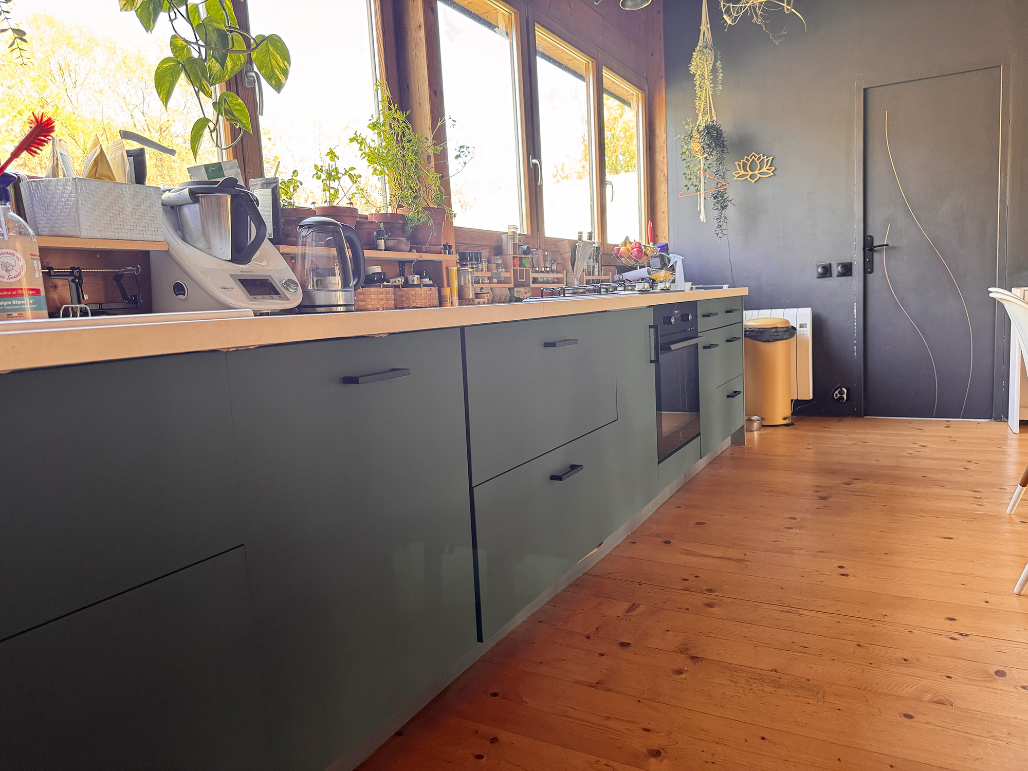 Le contraste entre les façades vertes, le plan de travail clair et les nombreux éléments en bois crée une ambiance naturelle, chaleureuse et très actuelle.