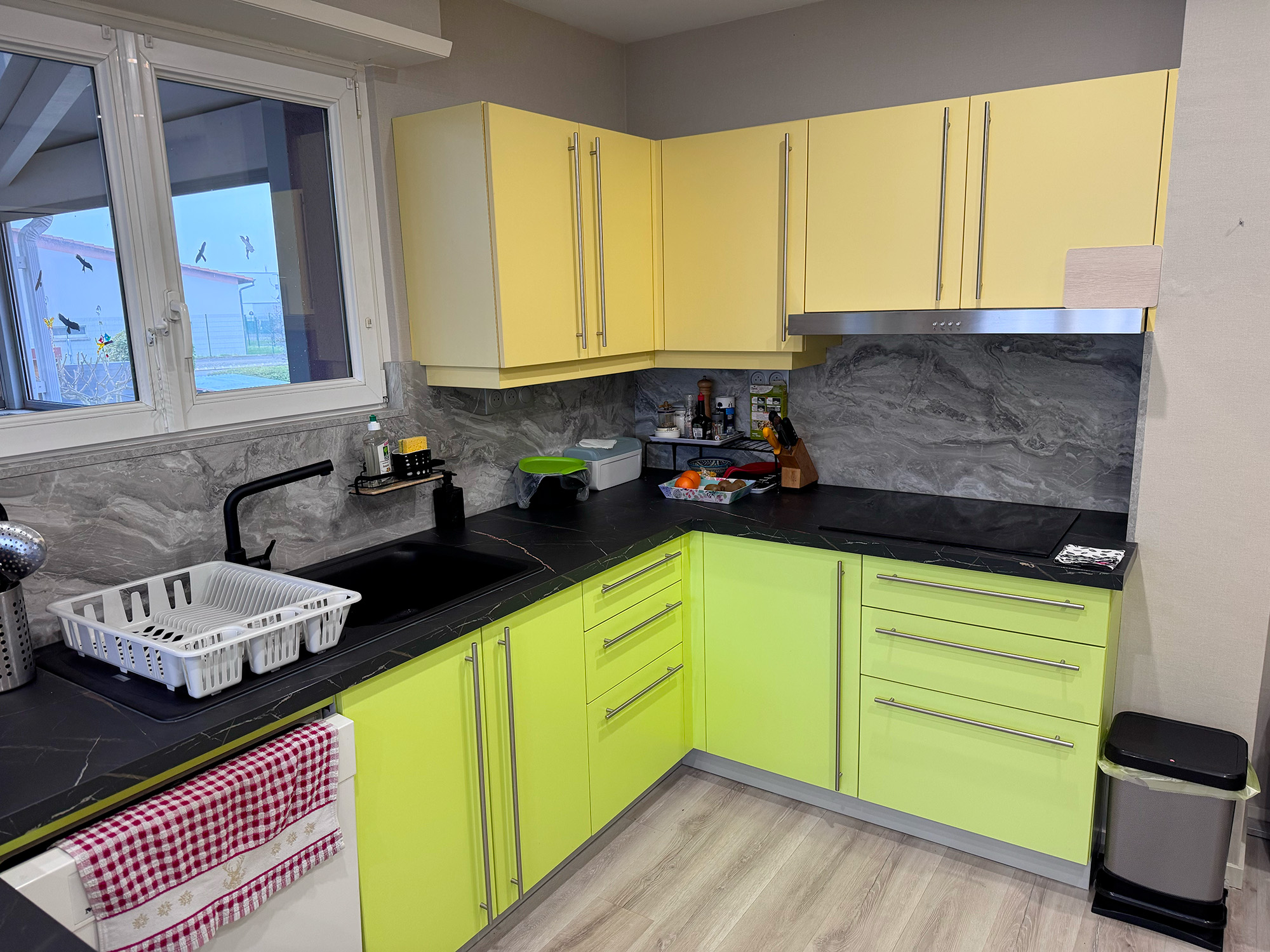 Avant sa transformation, cette cuisine associait des façades vert anis et jaune pâle, un style très marqué qui ne correspondait pas aux attentes de son nouveau propriétaire. Le covering architectural lui a offert une toute nouvelle identité, plus chaleureuse et intemporelle.